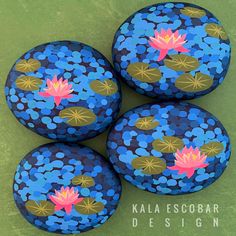 four painted rocks with water lilies on them sitting on a green surface, one is blue and the other is pink