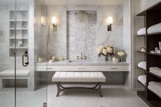 a bathroom with marble walls and flooring, white towels on the shelves and a bench in front of it