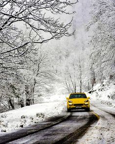 a yellow car driving down a snow covered road in the middle of trees and bushes