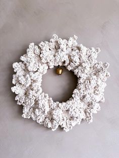 a white crocheted wreath with a gold bell hanging from the center on a gray wall