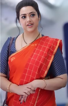 a woman in an orange and blue sari is standing with her hands on her hips