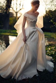 a woman in a white wedding dress is standing by the water