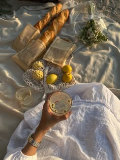 a woman is holding a plate with lemons and bread on it, while sitting in the sand