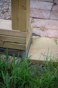 a piece of wood sitting on the ground next to some grass and bricks in front of it