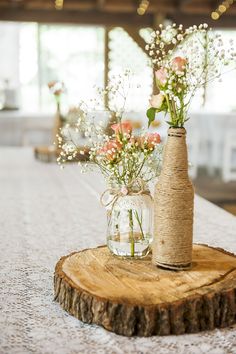 two vases with flowers are sitting on a wood slice at the end of a table