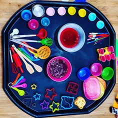 a child's play tray filled with different types of paints and spoons on top of a wooden table