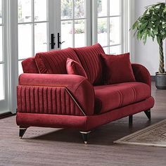 a red couch sitting on top of a wooden floor next to a potted plant