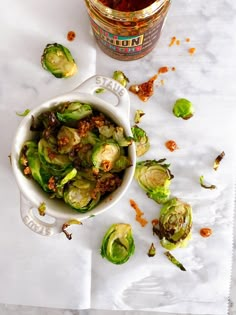 brussel sprouts in a white bowl next to a jar of sauce