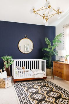 a white crib in front of a blue wall with a round mirror above it