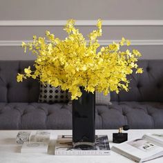 yellow flowers are in a black vase on a coffee table with books and magazines nearby