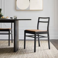 a dining room table with two chairs and a painting on the wall behind it,