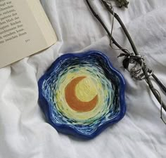 a blue bowl sitting on top of a bed next to an open book