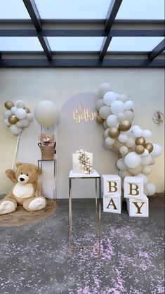 a teddy bear sitting next to a table with balloons in the shape of letters on it