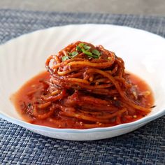 a white bowl filled with spaghetti on top of a blue table cloth covered in sauce