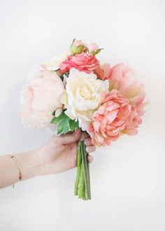 a bouquet of flowers being held by a woman's hand on a white background