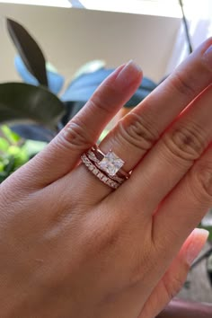 a woman's hand with two wedding bands on her fingers, and the other hand holding an engagement ring