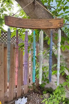 a wind chime hanging from a tree next to a wooden fence with green leaves