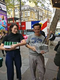 two people are standing on the sidewalk with some food in their hands and one is holding a cake