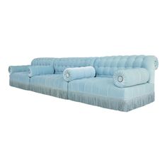 a light blue couch with fringe trim and pillows on the back, in front of a white background