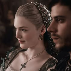 a man and woman dressed in medieval clothing, one wearing a tiara while the other wears an elaborate necklace