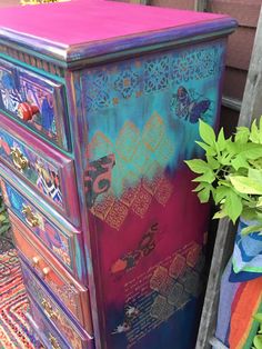 a colorful painted dresser next to a potted plant