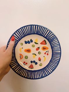 a person holding a plate with fruit on it and pointing to the side, in front of a white wall