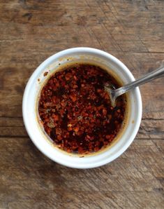 a white bowl filled with chili sauce on top of a wooden table next to a spoon