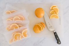 sliced oranges on a cutting board next to a knife and plastic bags with them