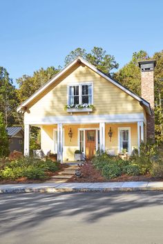 a yellow house with white trim on the front door and two windows, surrounded by trees