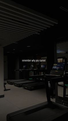 an empty gym room with treadmills and exercise equipment in the dark, while people watch on television