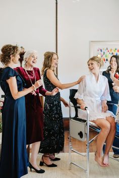 four women are laughing and having fun in the living room while one woman sits on a chair