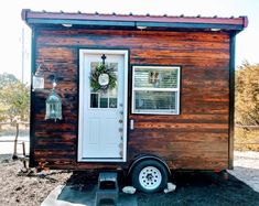 the tiny house is made out of wood and has a white front door with a wreath on it