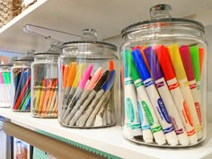 there are many different colored markers in the glass jars on the shelf next to each other