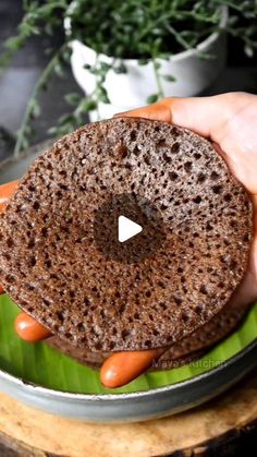 a person is holding a chocolate donut on a plate