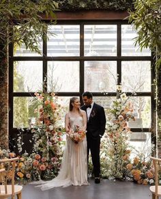 a newly married couple standing in front of an arch with flowers and greenery on it