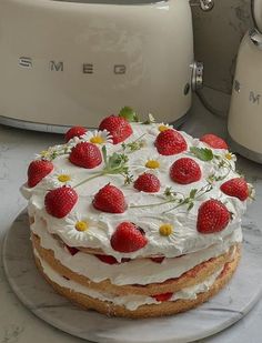 a cake with strawberries and daisies is on a plate next to two toasters