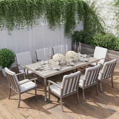 an outdoor dining table and chairs set up on a deck with greenery in the background