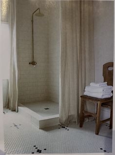 a bathroom with a stand up shower next to a wooden chair and white tiled floor