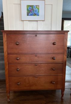 a wooden dresser sitting in front of a painting on the wall next to a stair case