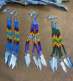 three pairs of beaded earrings with feathers hanging from them