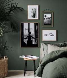 a bedroom with green walls and pictures hanging on the wall above it, along with a small side table