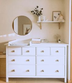 a white dresser with drawers and a mirror on the wall above it in a bedroom