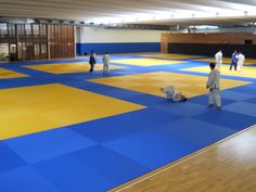 several people are practicing karate in an indoor gym with blue and yellow tiles on the floor