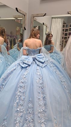 a woman in a blue ball gown looking at herself in the mirror