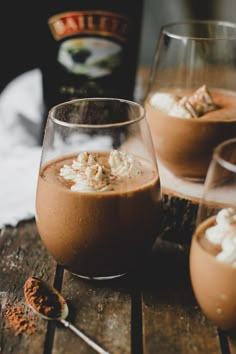 three glasses filled with dessert sitting on top of a wooden table