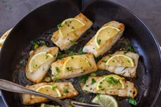 fish and lemons cooking in a skillet with a serving utensil on the side