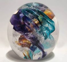 a glass ball that is sitting on a white surface with blue, yellow and purple swirls