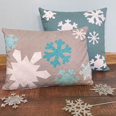 two pillows with snowflakes on them sitting on top of a wooden table next to each other