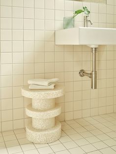 a bathroom with white tiles and a pedestal sink in the corner next to a stack of towels