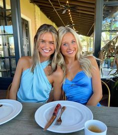 two beautiful young women sitting at a table with food